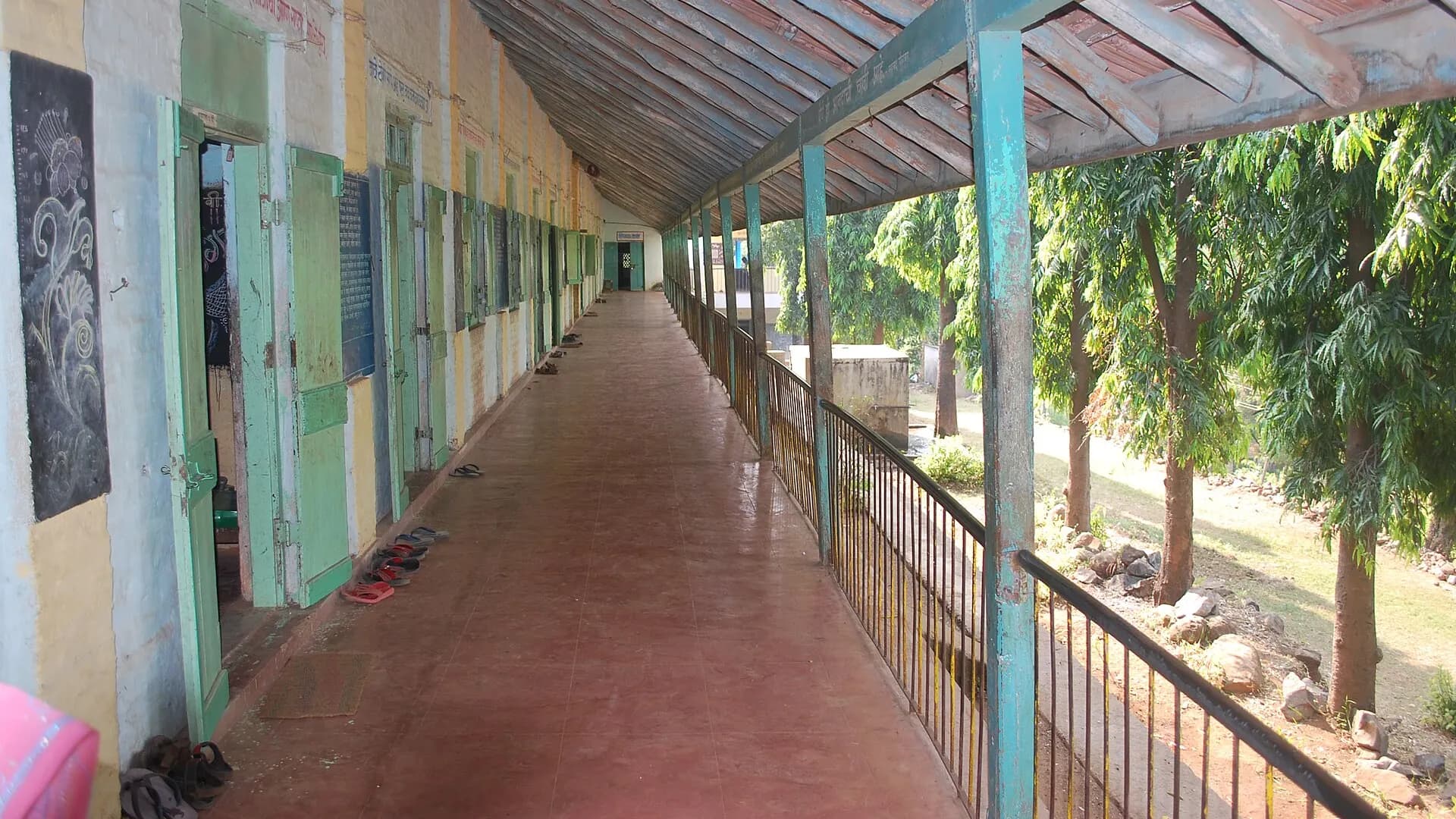 The open veranda of a village government school, classroom doors along one side and sandals left outside them