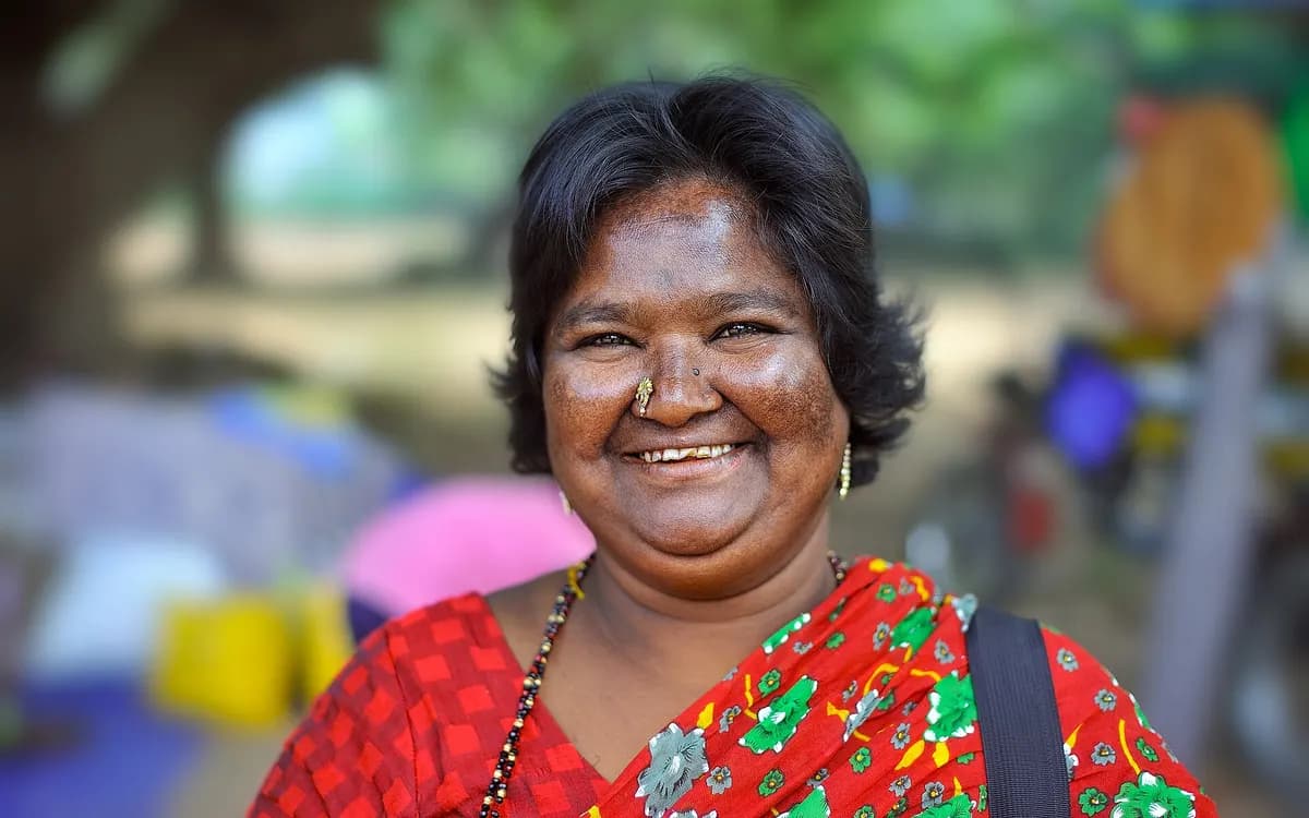 A woman in a red sari smiling, standing outdoors at a roadside market